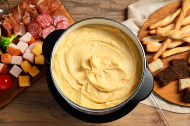 Photo of Tasty melted cheese in fondue pot and snacks on wooden table, flat lay