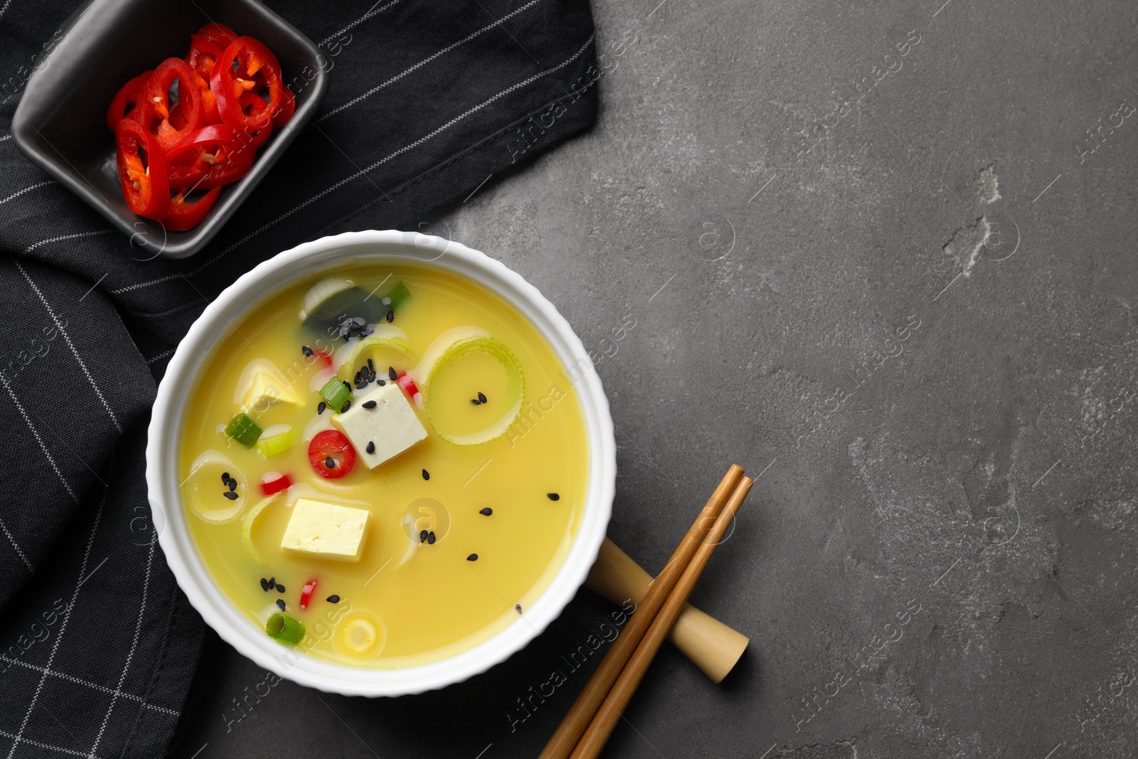 Photo of Bowl of delicious miso soup with tofu served on grey table, flat lay. Space for text