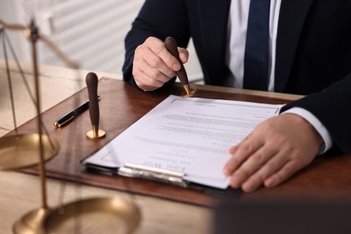 Photo of Notary stamping document at wooden table in office, closeup