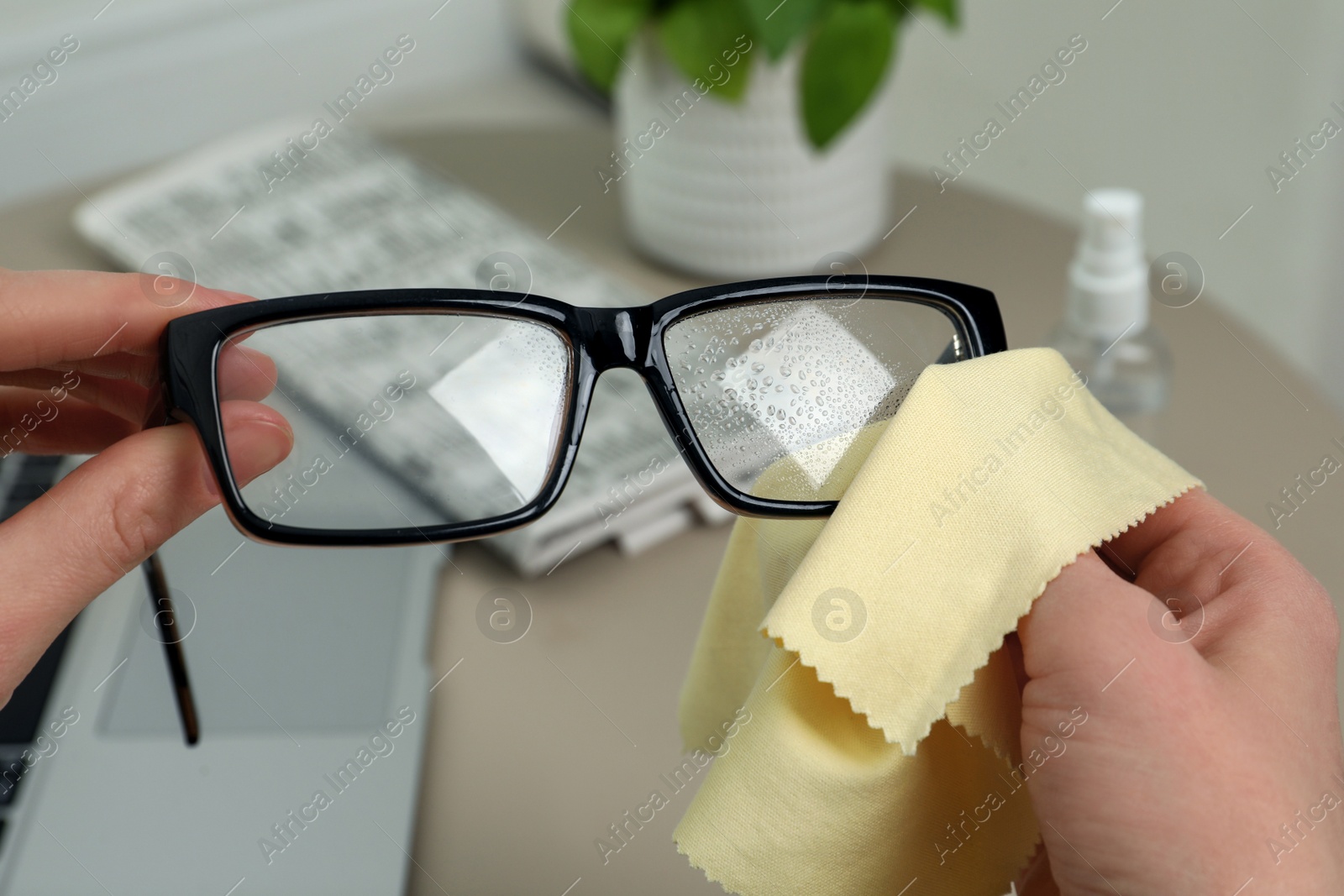 Photo of Woman cleaning glasses with microfiber cloth at home, closeup