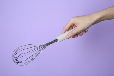 Woman holding metal whisk on lilac background, closeup