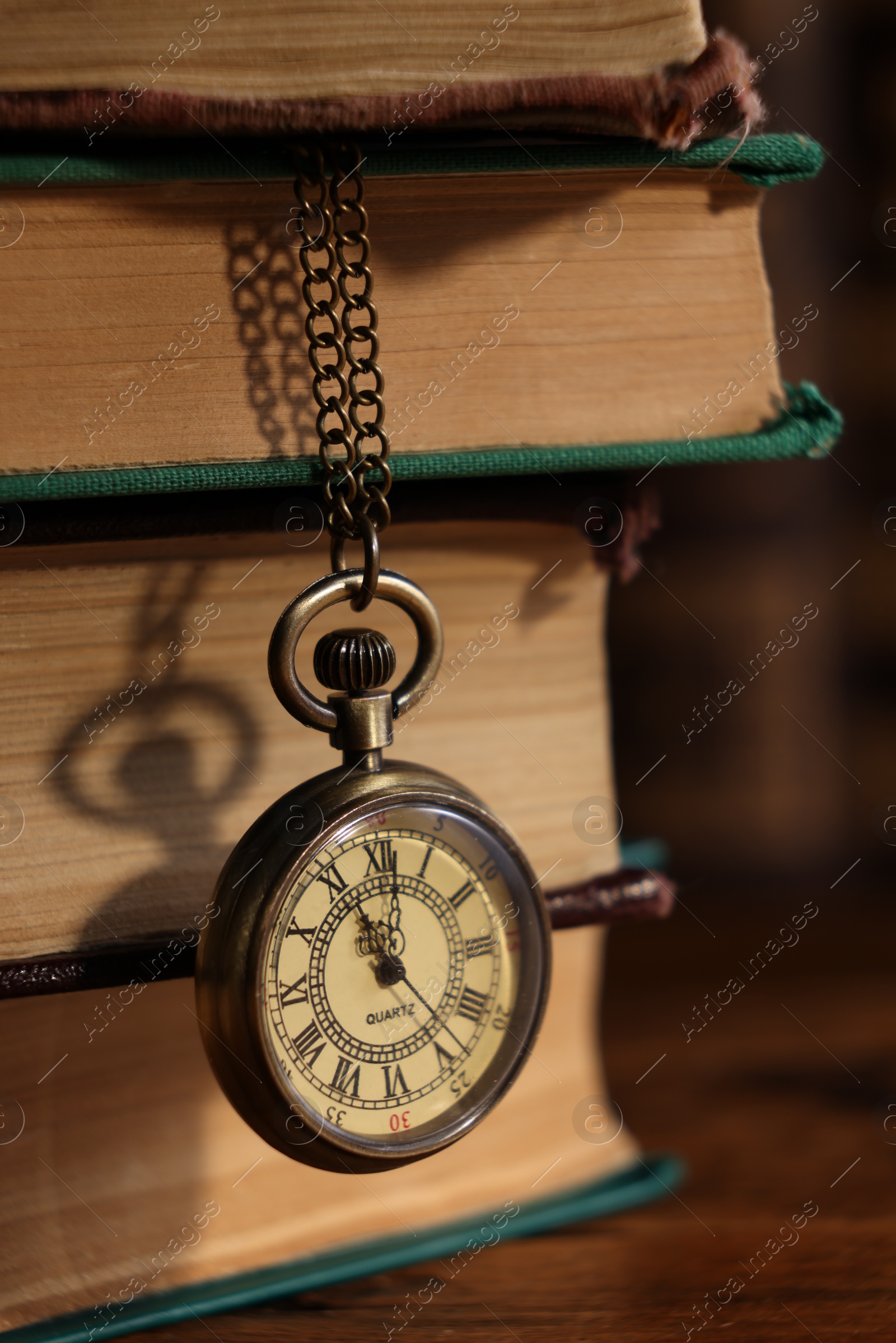 Photo of Pocket clock hanging on stack of books at table, closeup