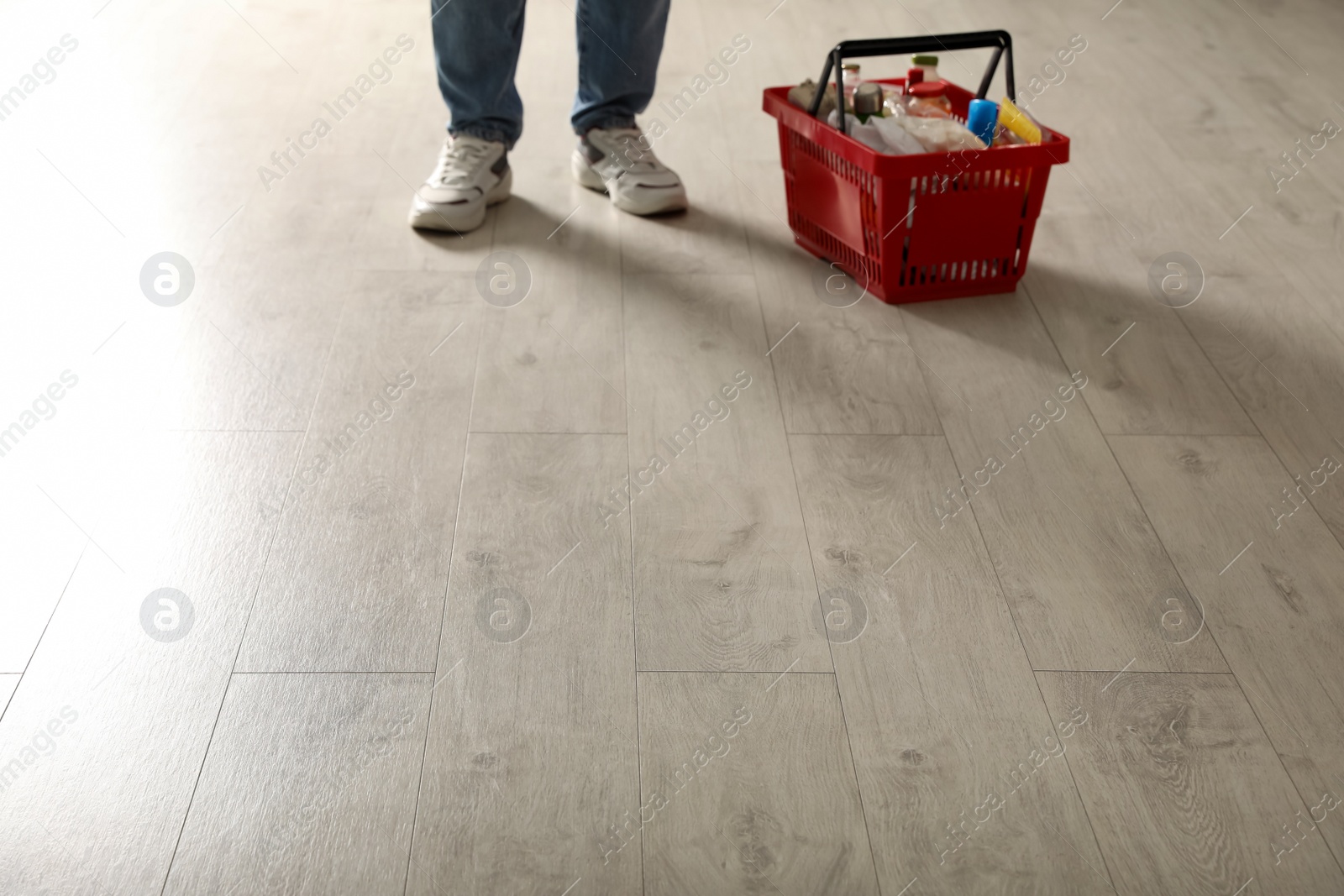 Photo of Woman and shopping basket with groceries on wooden floor, closeup. Space for text