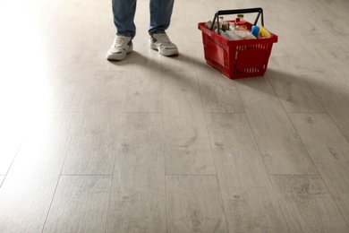 Photo of Woman and shopping basket with groceries on wooden floor, closeup. Space for text