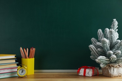 Photo of Christmas decor and school supplies on wooden table near chalkboard, space for text. Winter holidays concept