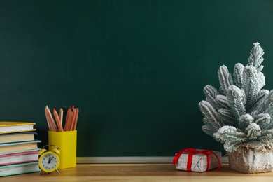 Christmas decor and school supplies on wooden table near chalkboard, space for text. Winter holidays concept