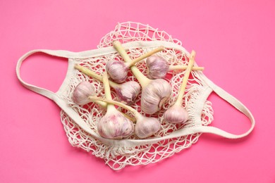 Photo of String bag with garlic heads on bright pink background, top view