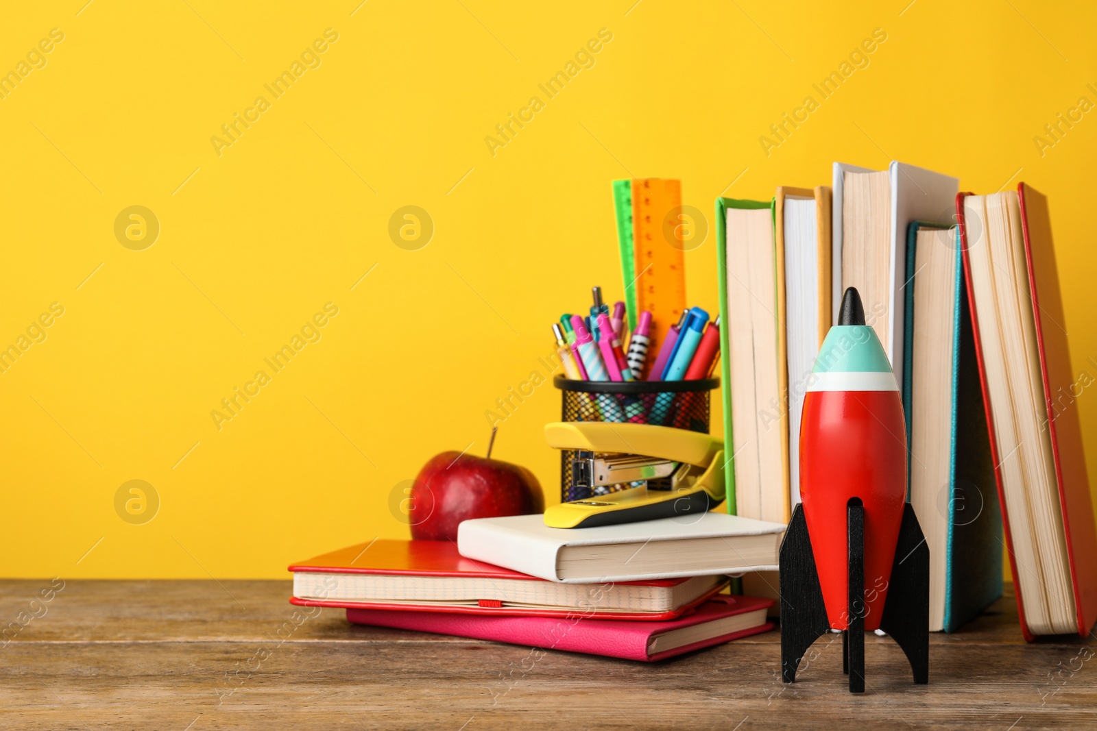 Photo of Bright toy rocket and school supplies on wooden desk. Space for text