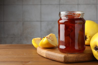 Tasty homemade quince jam in jar and fruits on wooden table, closeup. Space for text