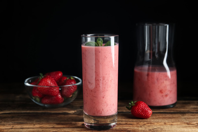 Photo of Tasty strawberry smoothie with mint in glass on wooden table