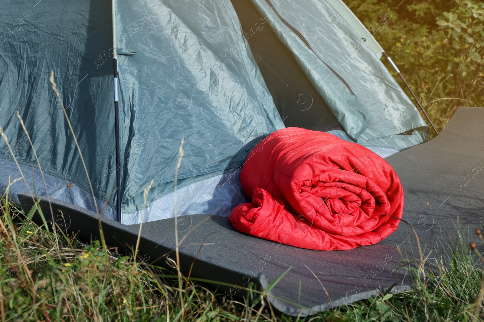 Photo of Red sleeping bag near camping tent on green grass outdoors