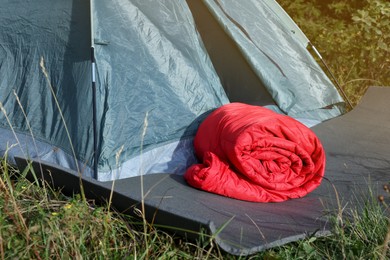 Photo of Red sleeping bag near camping tent on green grass outdoors