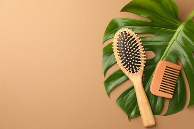 Wooden hairbrush, comb and green leaf on light brown background, flat lay. Space for text