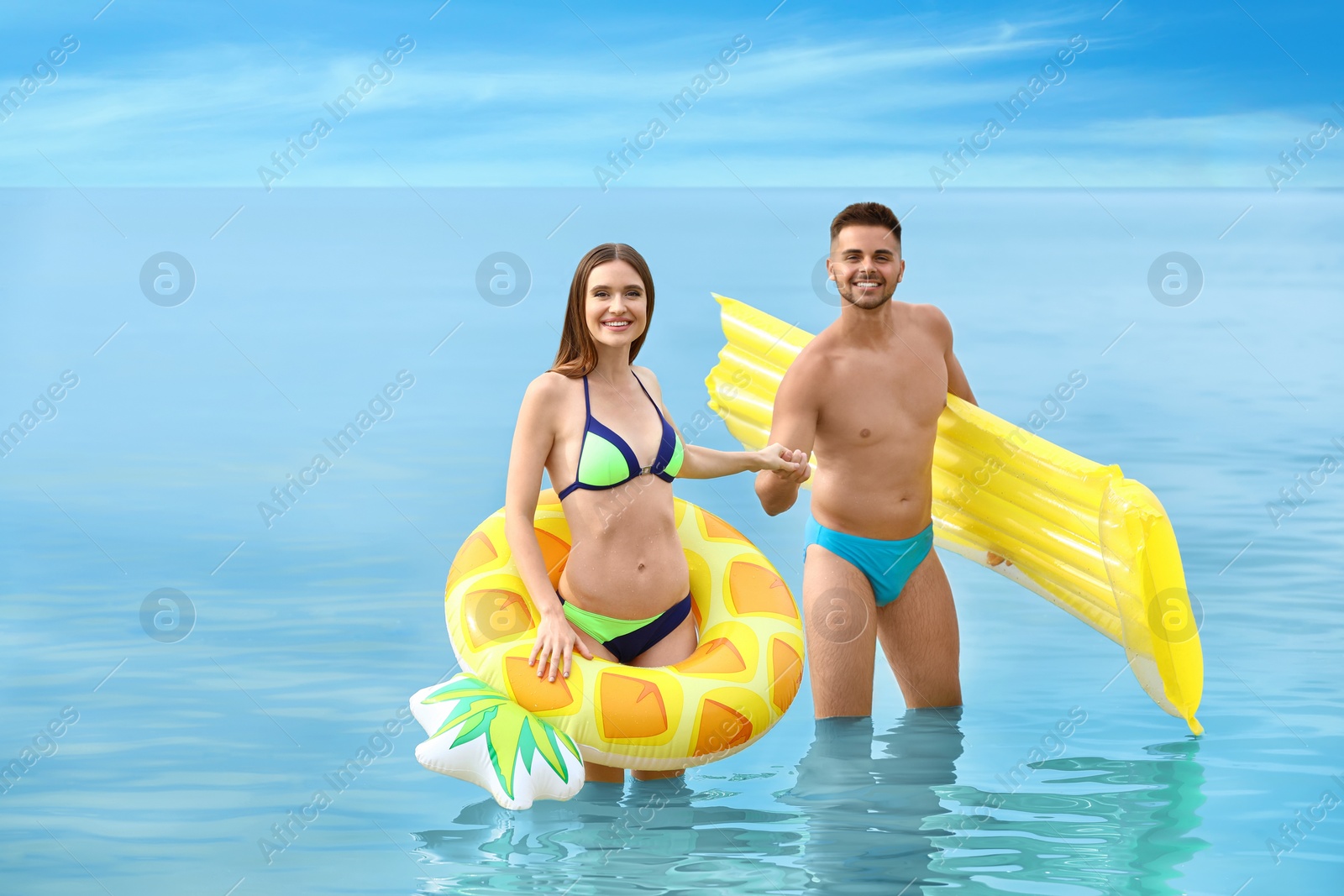 Photo of Young woman in bikini and her boyfriend with inflatable toys on beach. Lovely couple