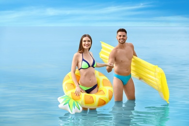 Young woman in bikini and her boyfriend with inflatable toys on beach. Lovely couple