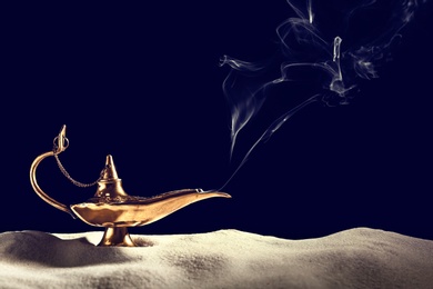 Photo of Aladdin magic lamp on sand against black background