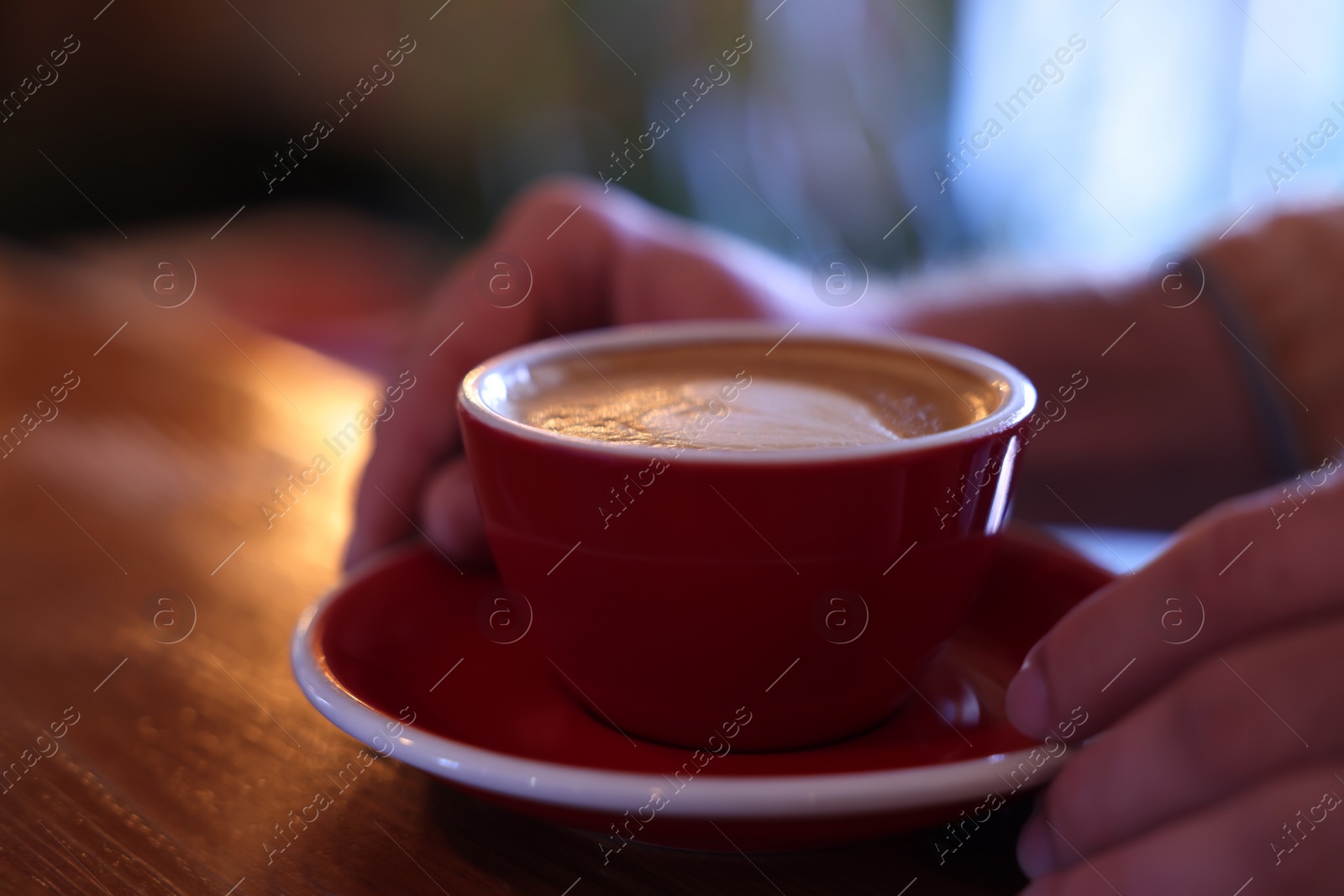 Photo of Man with cup of aromatic coffee at wooden table in cafe, closeup
