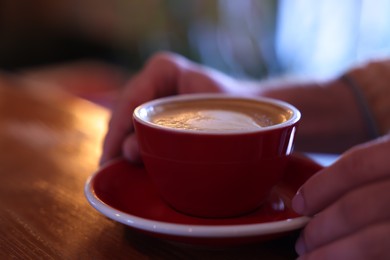 Man with cup of aromatic coffee at wooden table in cafe, closeup