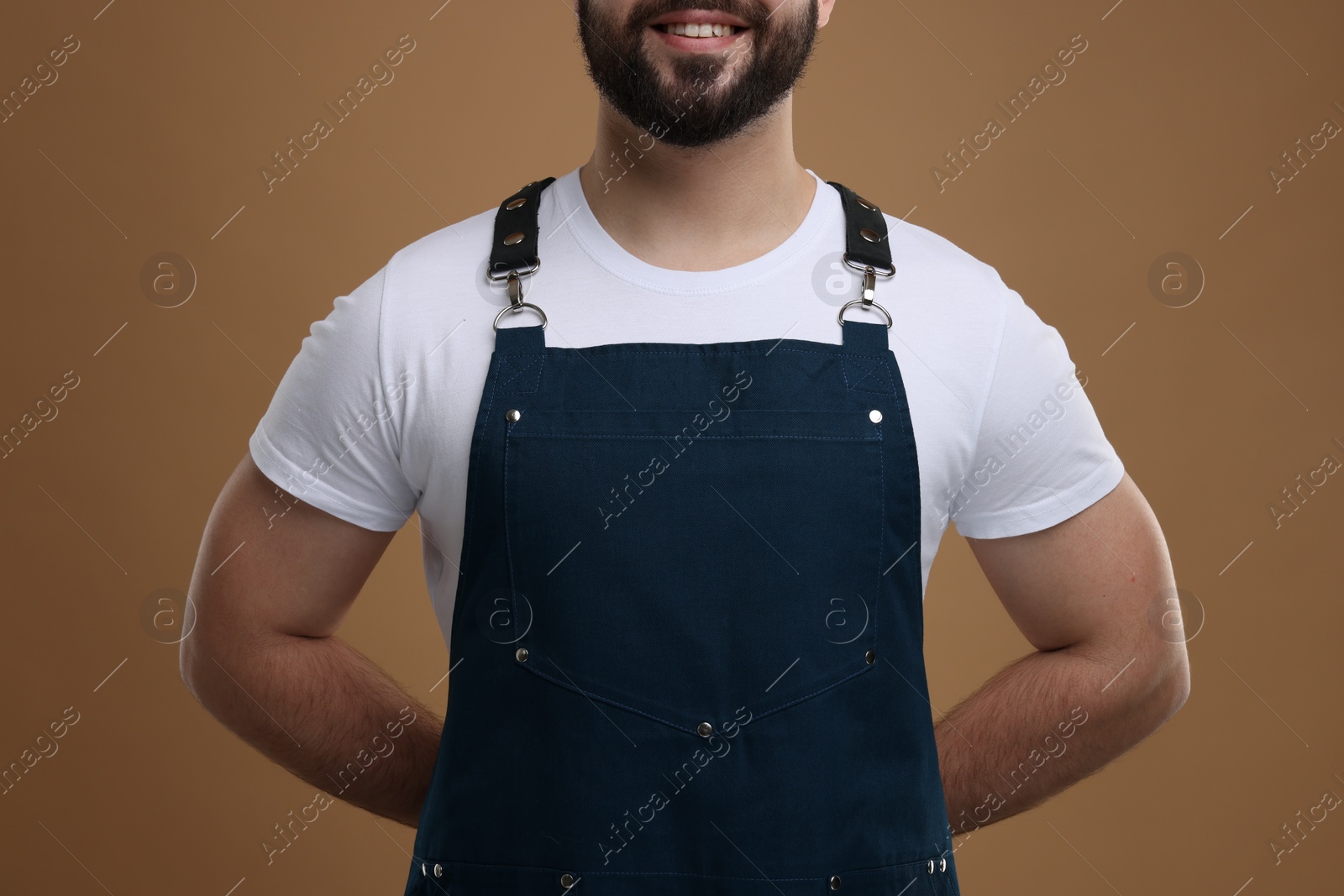 Photo of Smiling man in kitchen apron on brown background, closeup. Mockup for design