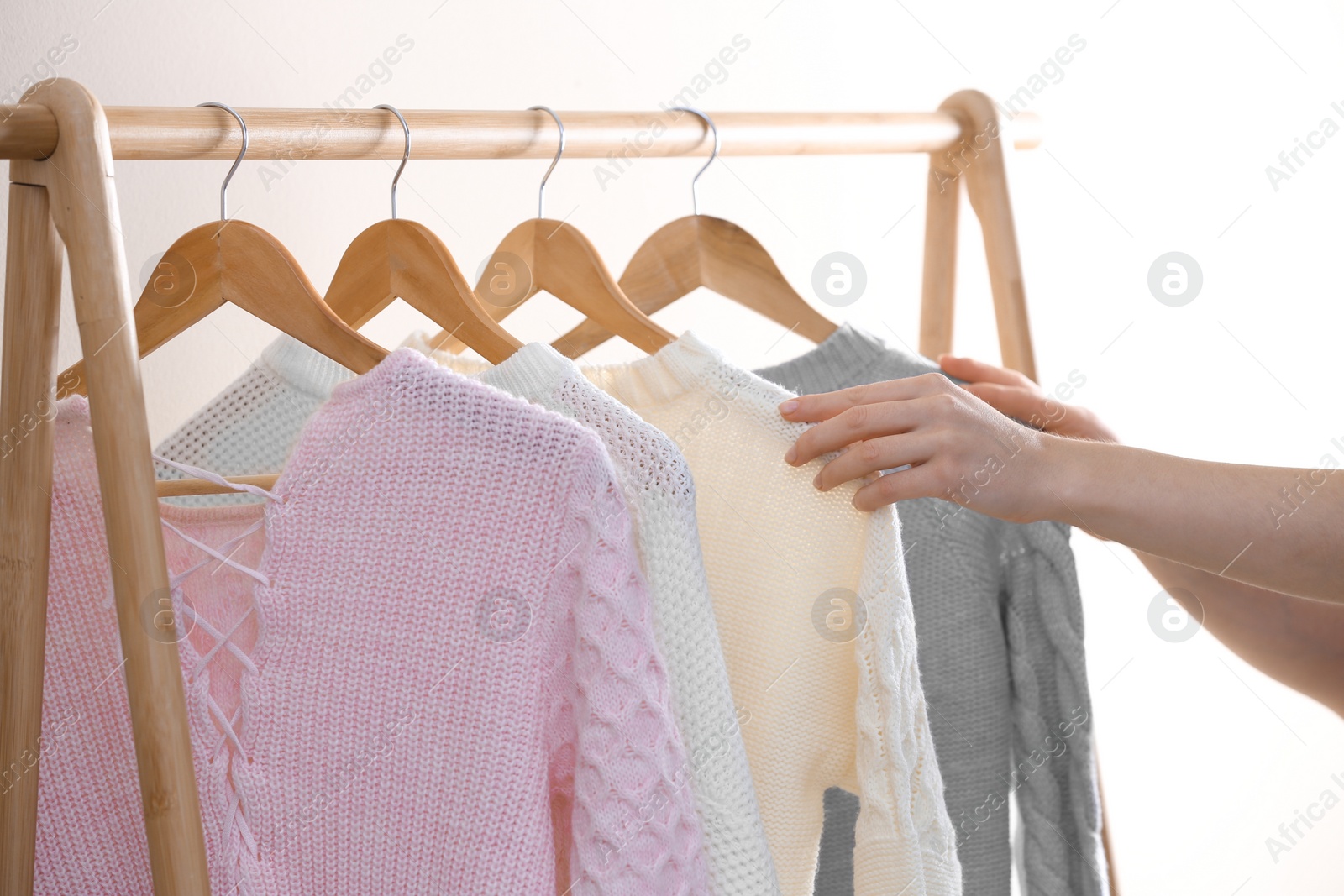 Photo of Woman choosing warm sweater on rack near light wall, closeup