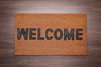 Photo of Stylish door mat with word Welcome on wooden floor, top view