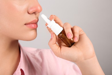 Photo of Woman using nasal spray on light grey background, closeup. Space for text