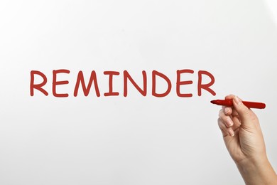 Image of Woman writing word REMINDER on glass against white background, closeup