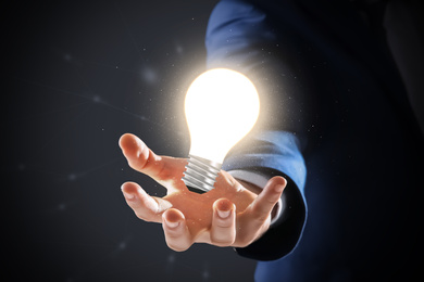 Image of Idea concept. Businessman demonstrating glowing light bulb illustration on dark background, closeup