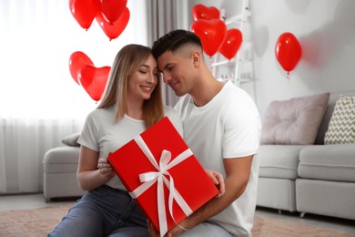 Photo of Lovely couple with gift in room. Valentine's day celebration