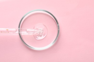 Glass pipette and petri dish with liquid on pink background, top view. Space for text