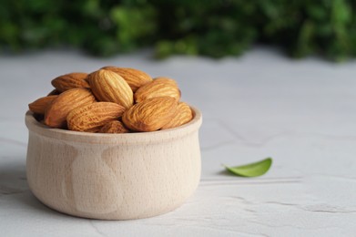 Tasty almonds in wooden bowl on white table, space for text