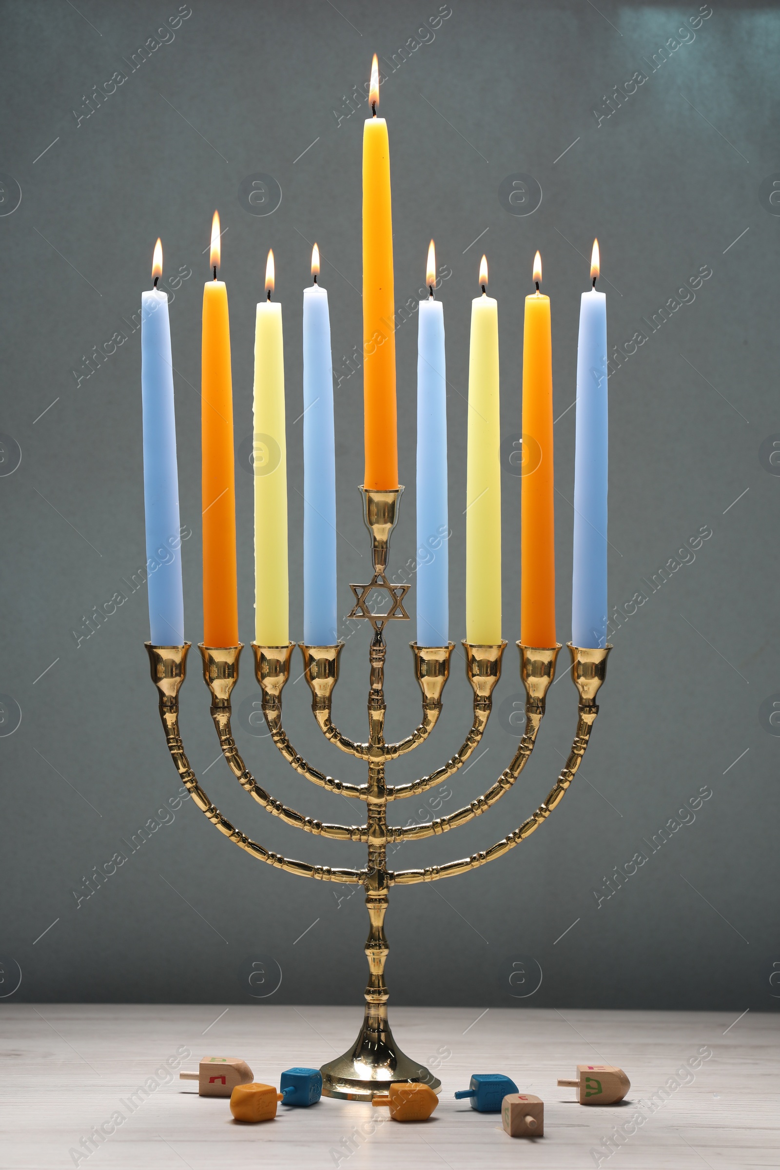 Photo of Hanukkah celebration. Menorah with burning candles and dreidels on light wooden table against grey background, closeup