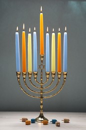 Photo of Hanukkah celebration. Menorah with burning candles and dreidels on light wooden table against grey background, closeup