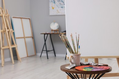 Photo of Wooden easel with canvas near paints, palette and brushes in artist's studio, space for text
