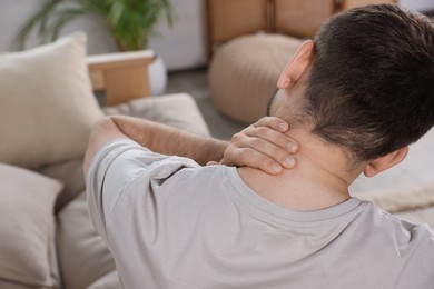 Photo of Man suffering from neck pain in living room, back view