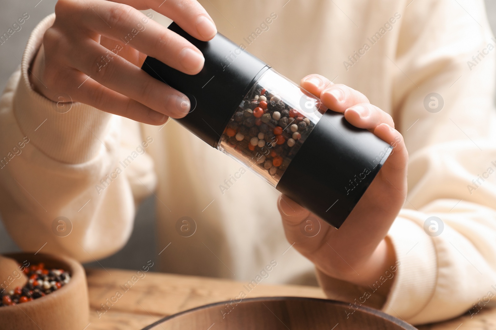 Photo of Woman grinding pepper with shaker at wooden table, closeup