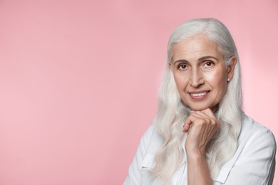 Portrait of beautiful mature woman on pink background, space for text