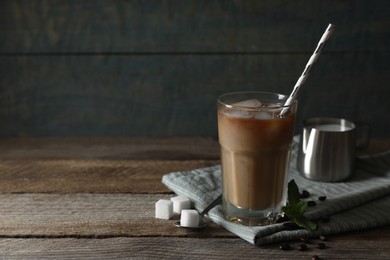 Photo of Glass of delicious iced coffee with milk, beans and sugar cubes on wooden table, space for text