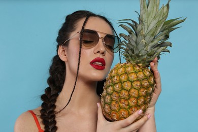 Young woman with fresh pineapple on light blue background. Exotic fruit