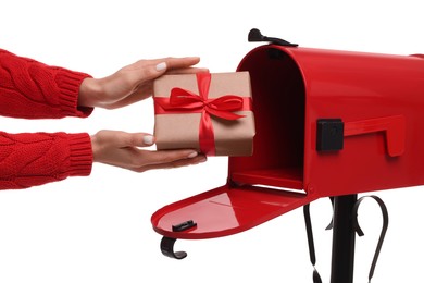 Woman putting Christmas gift into mailbox on white background, closeup. Sending present by mail