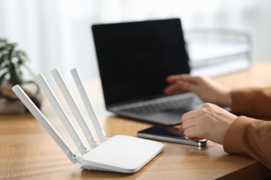 Photo of Woman with smartphone and laptop connecting to internet via Wi-Fi router at table indoors, closeup