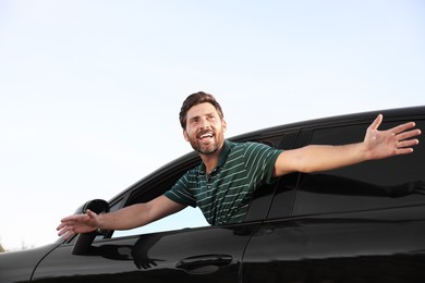 Enjoying trip. Happy man leaning out of car window outdoors, low angle view