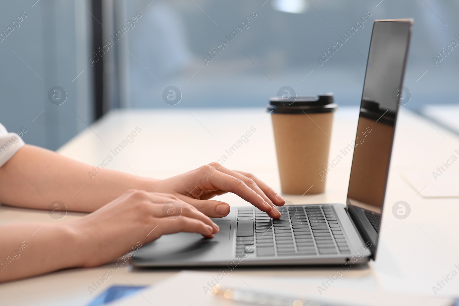 Photo of Woman working with laptop at white desk indoors, closeup