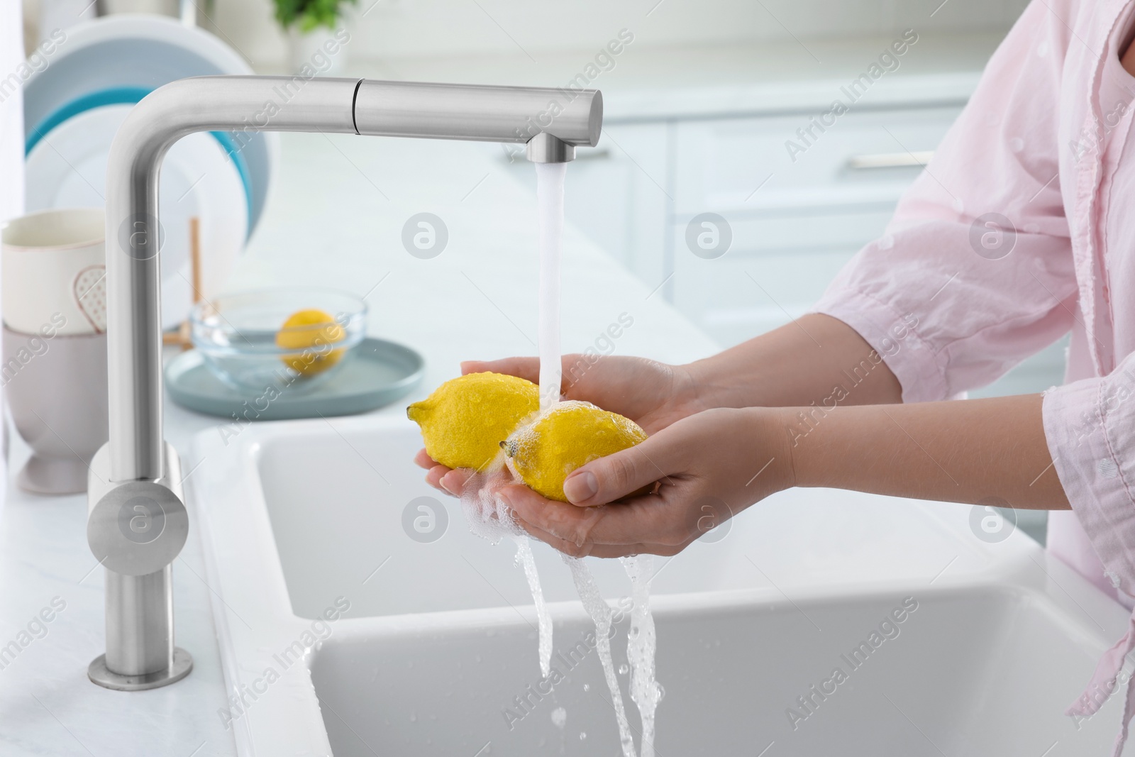 Photo of Woman washing fresh ripe lemons under tap water in kitchen, closeup