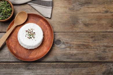 Plate of fresh cottage cheese with spice, microgreens and spoon on wooden table, flat lay. Space for text