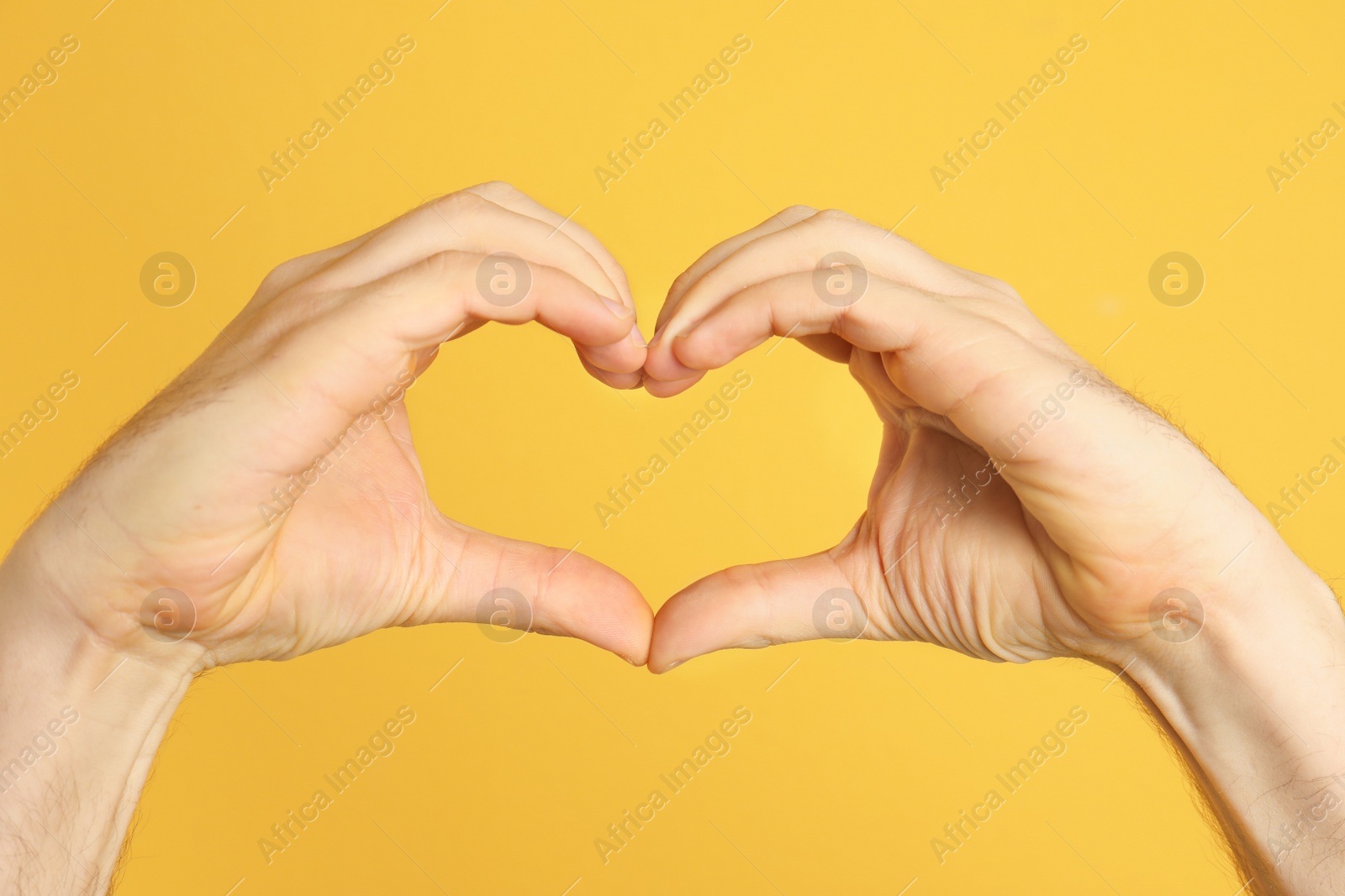 Photo of Man making heart with his hands on color background, closeup