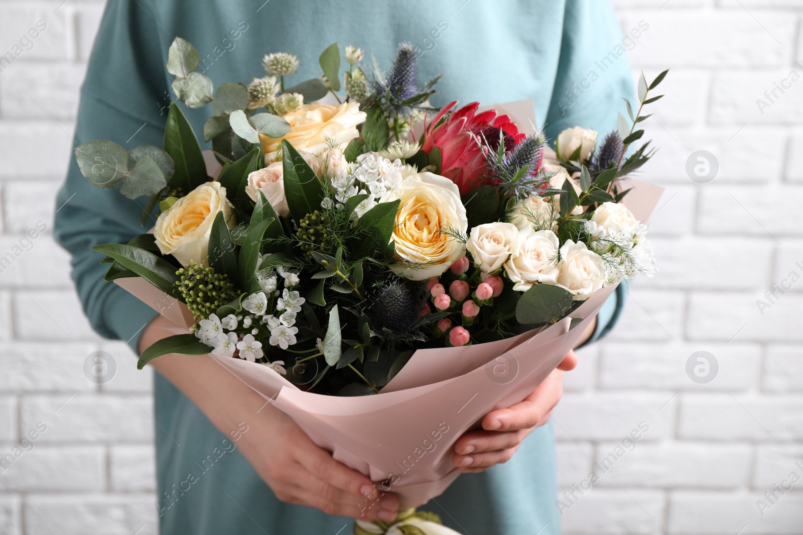 Photo of Woman with bouquet of beautiful roses near white brick wall, closeup