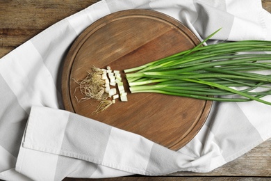 Photo of Wooden board with green spring onions and fabric on table, top view