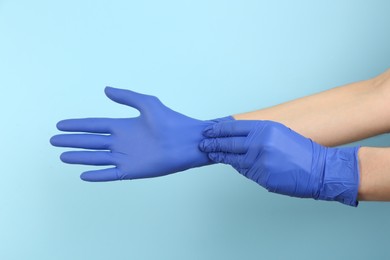 Photo of Person putting on medical gloves against light blue background, closeup of hands