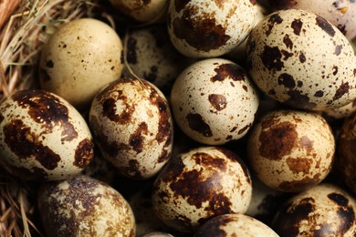 Photo of Whole speckled quail eggs and straw as background, top view